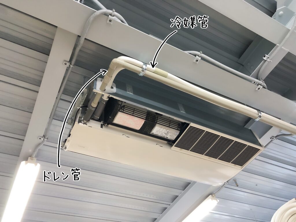 建設会社の天井に設置されたエアコンの写真です。ドレン管と冷媒管を説明する画像です。